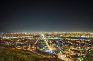從草坡上觀賞的廣闊城市夜景，帶有發光的燈光和交通軌跡。