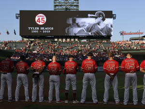 紅色球衣的棒球隊在夕陽下的球場向Tyler Skaggs致敬。