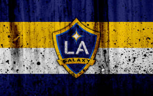 LA Galaxy足球隊標誌，背景為骯髒的藍色、黃色和白色條紋。 — 足球 壁紙