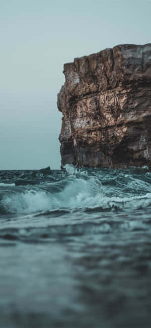 在暴風雨的海岸場景中，海浪拍打著高聳的懸崖面。