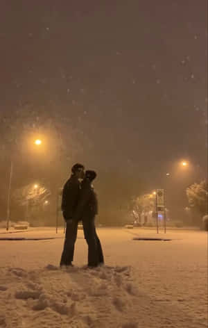 一對情侶在夜晚的路燈下，於飄雪中親吻。