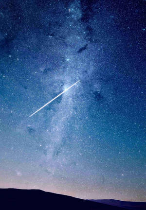 流星在沙漠剪影之上，劃過佈滿星星的夜空留下一道軌跡。