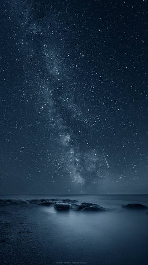 夜晚黑色海洋岩石上的銀河與流星