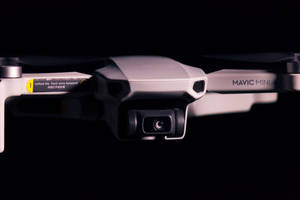 銀色DJI Mavic Mini無人機，帶相機和手臂指示，黑色背景。