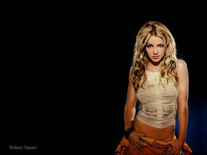 Britney Spears 身穿破爛的米色上衣和橙色裙子，背景為黑色。