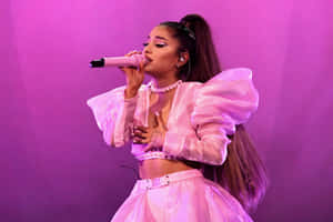 歌手Ariana Grande穿著粉紅色服裝在舞台上拿著麥克風表演。