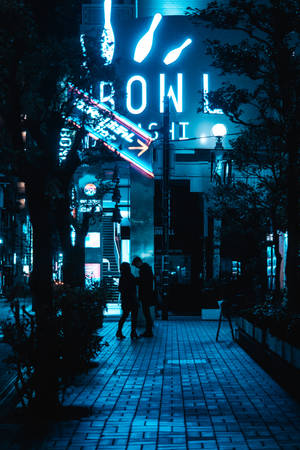 情侶在雨夜街道上霓虹燈招牌下行走。
