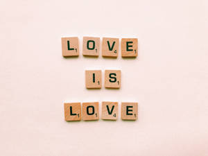木製Scrabble字母牌在米色表面上拼出「Love is Love」。 — 愛就是愛 壁紙