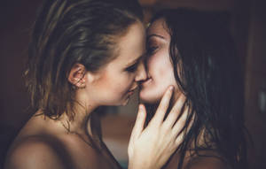 兩位濕髮女性在柔和照明的房間裡親密接吻。