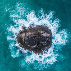 深色裂開的岩石被碧綠色的海浪拍打環繞 — 島嶼 壁紙