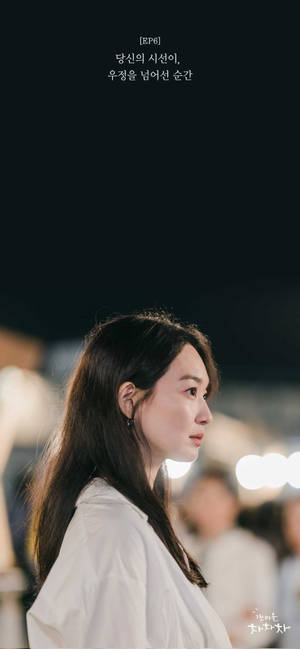 身穿白恤衫的女性凝視夜晚，若有所思，背後有模糊的城市燈光。 — 成振宇 壁紙