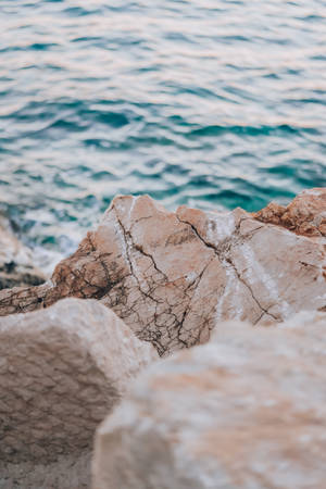 海邊的米色岩石帶有深色裂縫，背景是碧綠的海水。