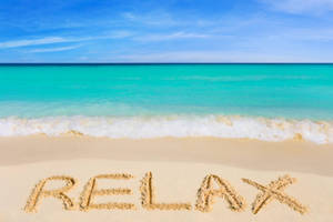 喺熱帶海灘嘅沙上寫住「relax」呢個字，有藍綠色海水同藍天。