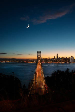 黃昏的海灣大橋，城市燈光與一彎新月。