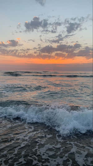 在色彩繽紛的夕陽下，海浪拍打著海岸，天空有散落的雲朵。