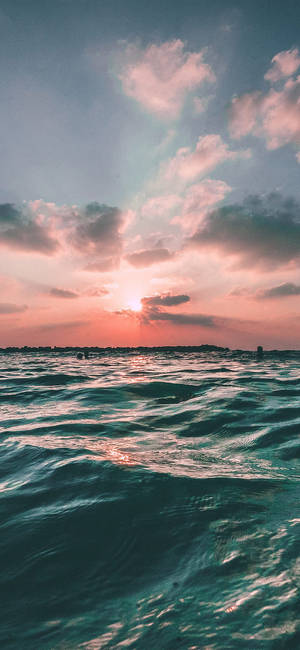 夕陽下的海洋，粉橙色天空和藍綠色水波紋 — iPhone 11 壁紙