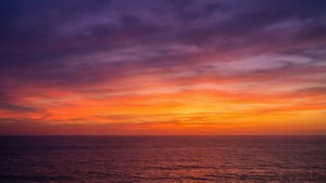平靜海洋上充滿活力的日落，紫色和橙色的雲彩倒映在水面上。 — 漸變色 壁紙