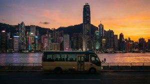 日落時分，黃色小巴在海濱道路上，背景是香港天際線。