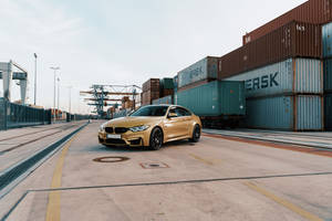 金色BMW M4雙門跑車停泊在集裝箱港口，有起重機和堆疊的集裝箱。