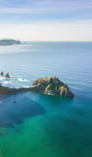 海岸島嶼，碧綠海水，有一座紅色屋頂的小建築。