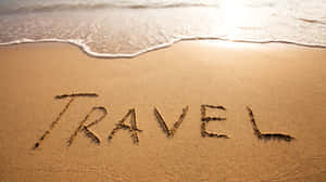 日落時分，海浪逼近，沙上寫住「travel」呢個字。