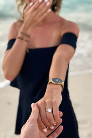 女性在海灘上與伴侶牽手時，因手指上的訂婚戒指而感到驚訝。