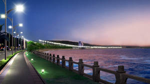 黃昏時分亮燈的海邊步道，遠方有海洋和城市燈光。