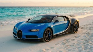 日落時白色沙灘上的藍色Bugatti Chiron與海浪。