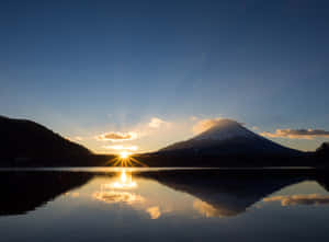 富士山在夕陽下倒映在平靜的湖中，周圍是黑暗的山坡。 — 日出 壁紙