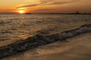 海洋上的夕陽，波浪沖刷海岸，遠處有船和燈塔。