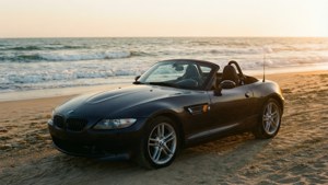 黑色BMW Z4開篷車停泊在沙灘上，夕陽下伴隨海浪。