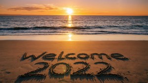 海洋上的日落，水邊沙灘上寫著「Welcome 2022」