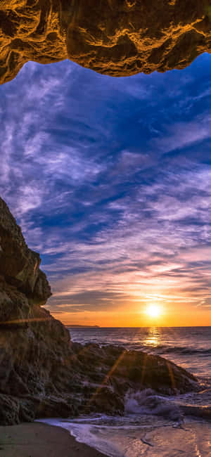 從岩石洞穴內部觀看的夕陽，俯瞰海洋。 — Redmi Note 14 Pro 壁紙