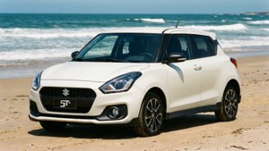 白色鈴木Swift ST停泊在沙灘上，有海浪和清澈天空。