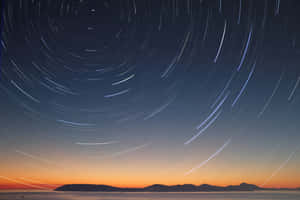 星軌在平靜的海面和山脈上空劃出弧線，時值黃昏。