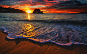 海洋上的夕陽，海浪沖刷沙灘和遠處的岩石島。