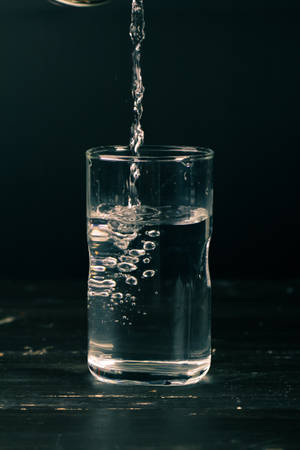 水倒入玻璃杯中，在深色表面上形成氣泡。