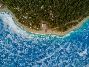 從高空俯瞰，一座小屋坐落在森林海灘上，碧綠色的海浪拍打著海岸。