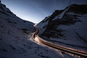 蜿蜒的積雪山路，黃昏時有汽車燈光軌跡。