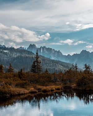 山湖映照鋸齒狀山峰和秋日樹木，天空多雲