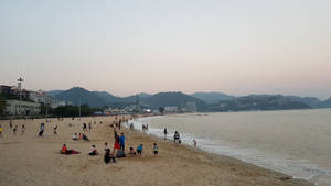 海灘遊客在擁擠的沙灘上欣賞日落，背景有山脈。 — 唐人街 GIF 壁紙