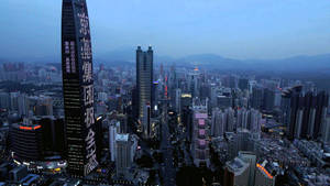 黃昏時分的城市天際線，燈火通明的摩天大樓和遠山。 — 唐人街 GIF 壁紙