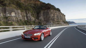 紅色BMW Z4開篷跑車在海岸公路上行駛，懸崖和海洋