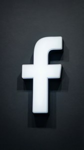 深色紋理牆壁上發光的白色Facebook標誌。