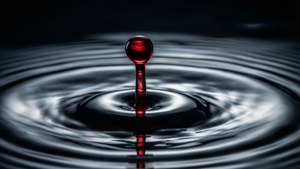 一顆紅色水滴懸浮在水面上，漣漪向外擴散。 — 血 壁紙