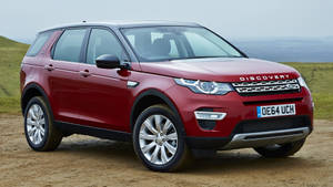 紅色Land Rover Discovery SUV停泊喺泥路上，後面有綠色山丘。 — 日間 壁紙