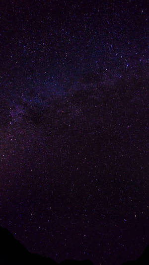 夜晚，黑暗山巒輪廓上方，銀河系呈現紫色和藍色星星。