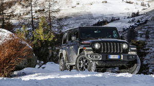 黑色Jeep Wrangler在雪覆蓋的山景中行駛。