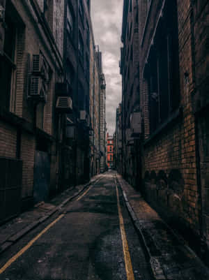磚建築之間狹窄的小巷，灰色天空，黃色道路標線。 — iPad Pro 13 壁紙