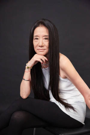 一位長黑髮的女士在攝影棚裡穿著白色上衣和黑色緊身褲靜靜地坐著。
